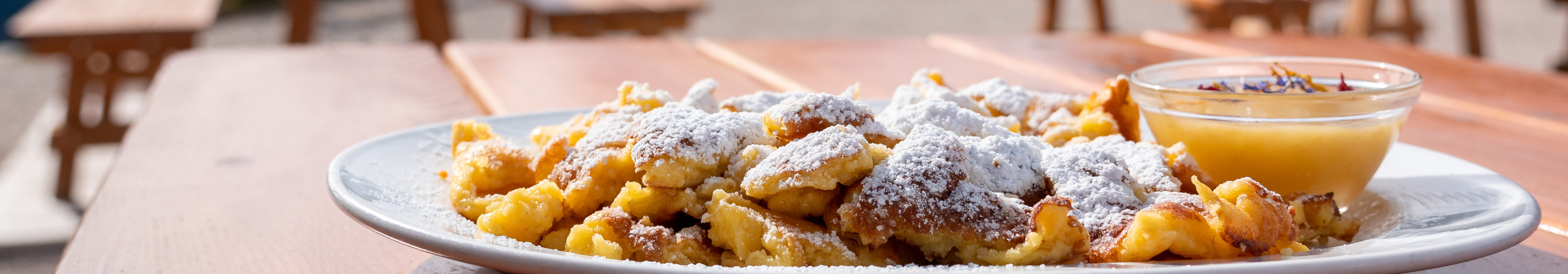 Teller mit Kaiserschmarrn und Apfelmus auf einer Berghütte, im Hintergrund die Dolomiten