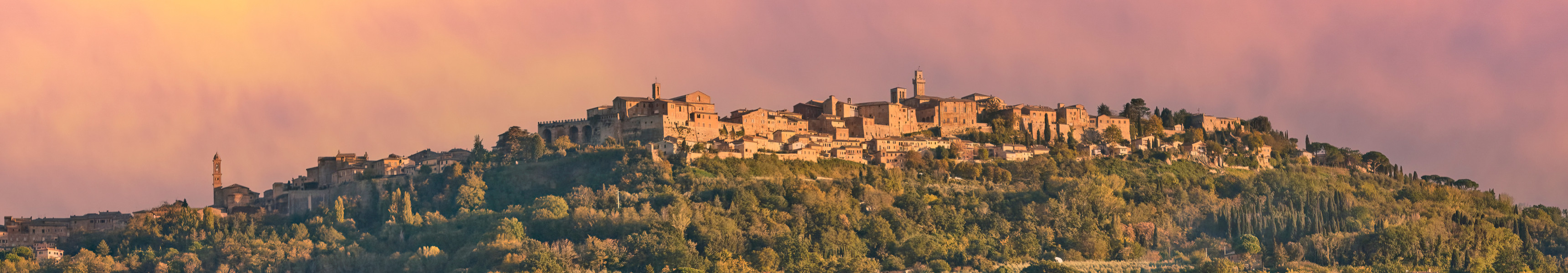 Radfahrerin auf einem Feldweg in der Toskana, Italien, im warmen Abendlicht; im Hintergrund liegt die historische Stadt Pienza.