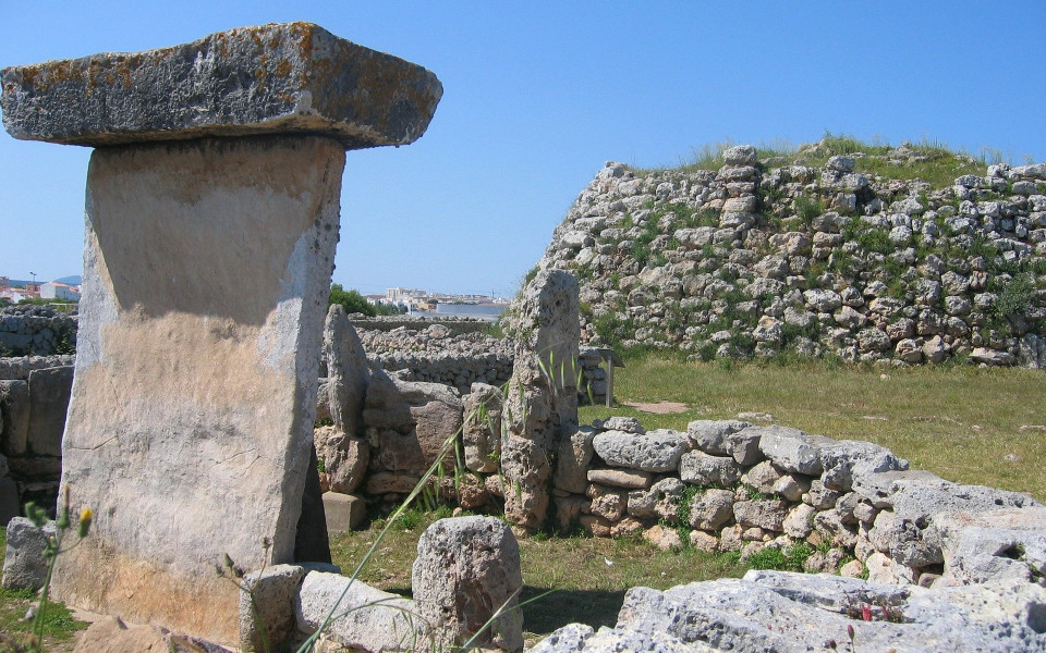 Pr&auml;historische Ruinen der Talayot-Kultur auf Menorca mit gro&szlig;en Steinen und Mauern, umgeben von einer gr&uuml;nen Landschaft und blauen Himmel.