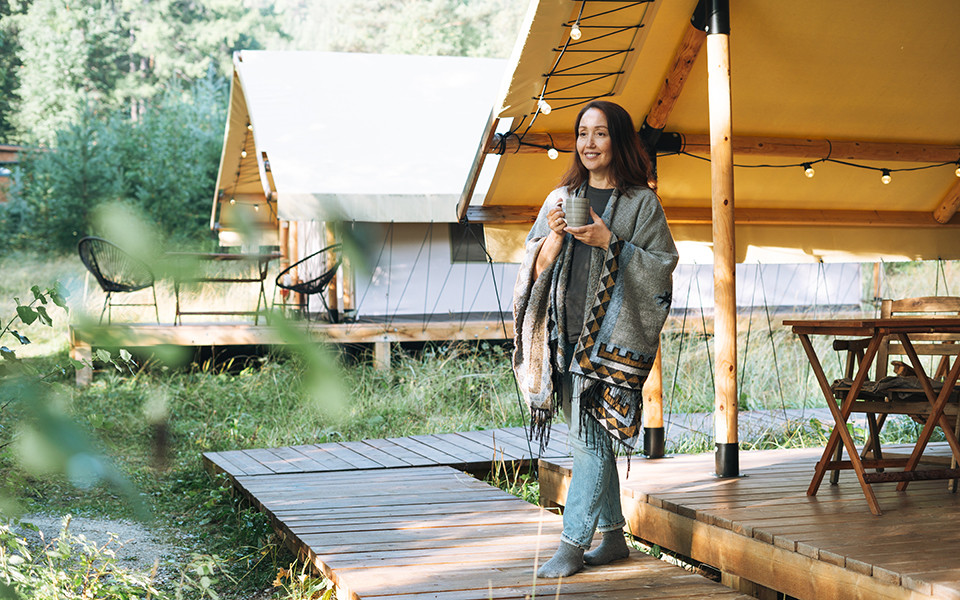 Frau mit Kaffeetasse vor einem Glamping-Zelt in der Natur