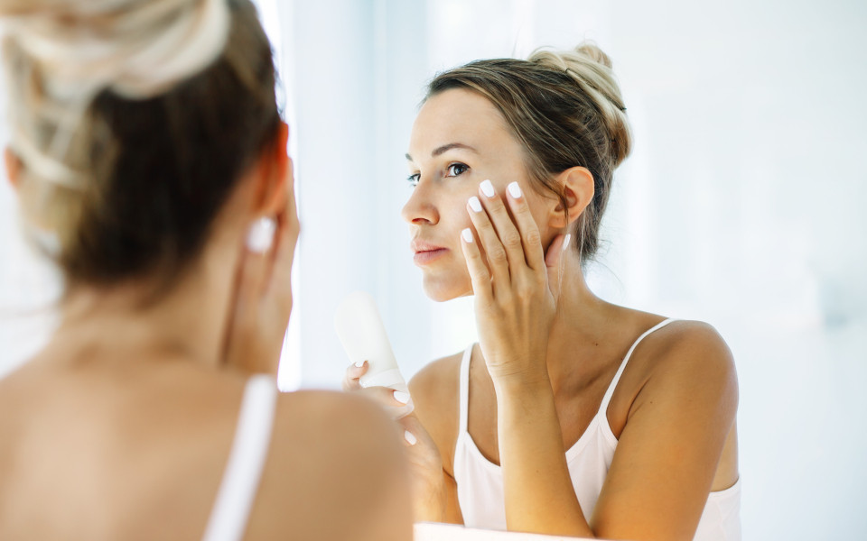 Frau cremt sich w&auml;hrend eines Langstreckenfluges das Gesicht vor dem Spiegel ein