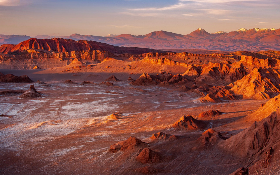 Trockene Felslandschaft im Valle de la Luna mit r&ouml;tlichen Gesteinsformationen und schneebedeckten Andengipfeln im Hintergrund.