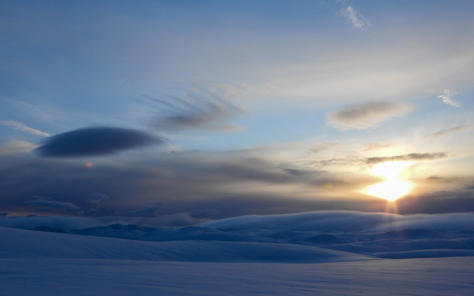 Nordkap im Winter mit einer schneebedeckten Landschaft und tief stehender Sonne über dem Horizont.
